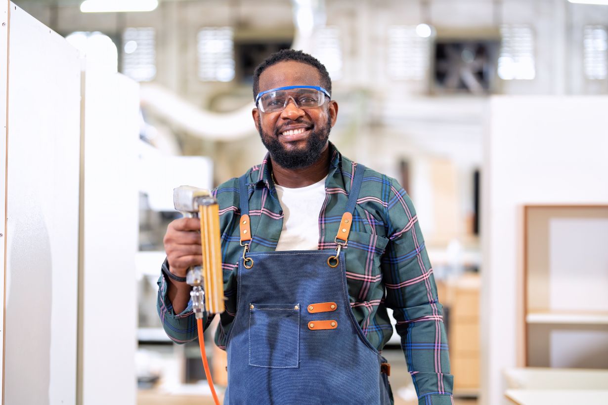 In work place carpenter man working using pneumatic nail gun stand portrait smiling